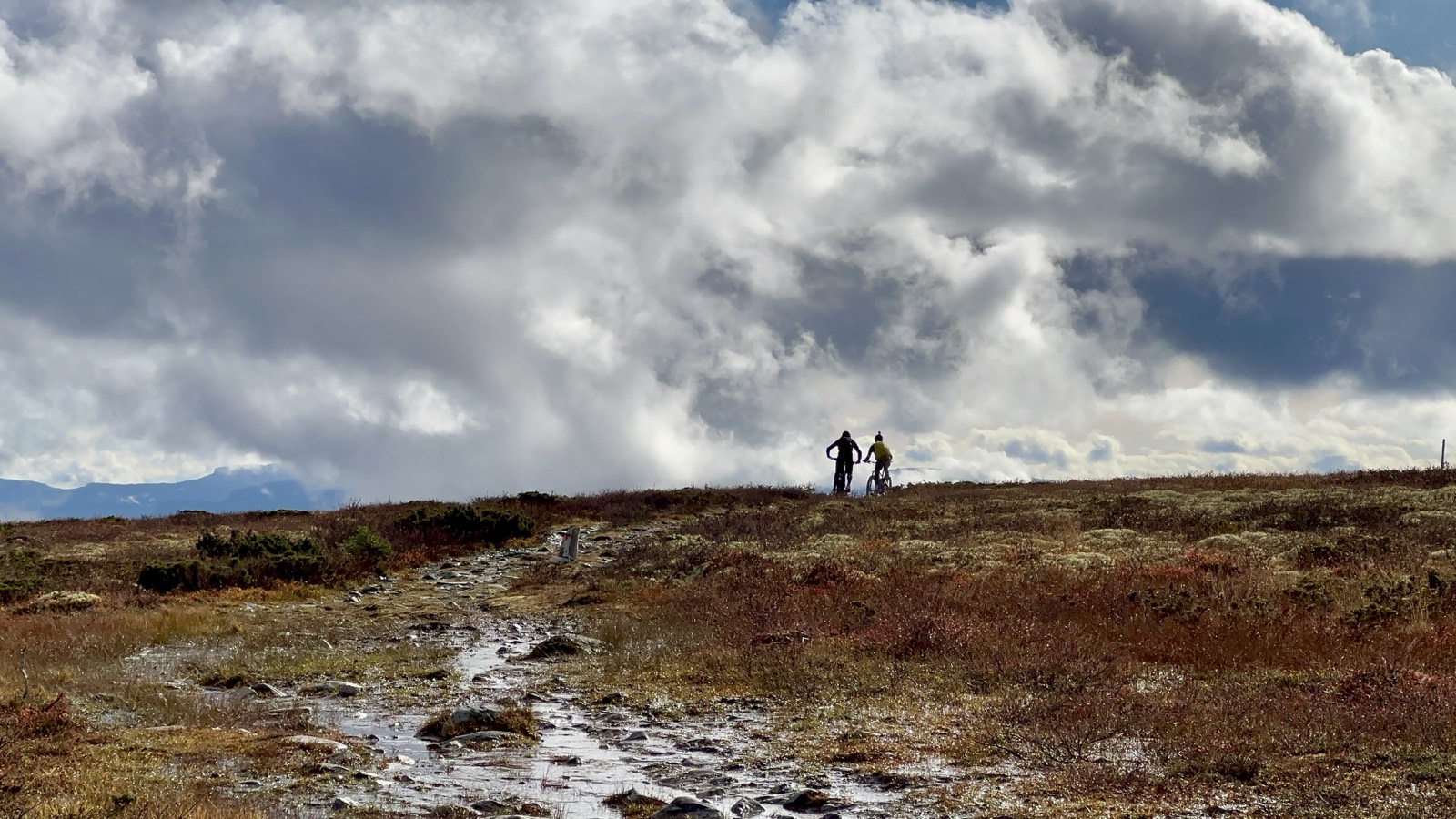 Twee e-mountainbikers rijden over een bergkam in de Noorse fjell bij Ringebu, onder een dramatische wolkenlucht